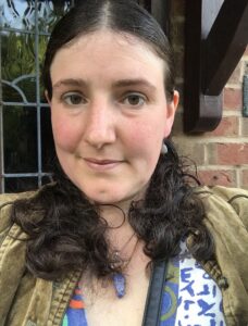 Someone with dark hair wearing a green jacket smiles at the viewer.