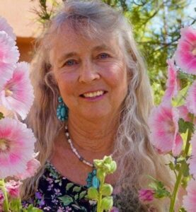 A woman with long hair smiling at the viewer surrouded by pink flowers.